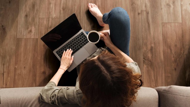 Gestalten Sie Ihr Zuhause mit Fliesen von KERAMUNDO Frau sitzt entspannt mit ihrem laptop auf dem Schoß auf dem Boden vor ihrem Sofa