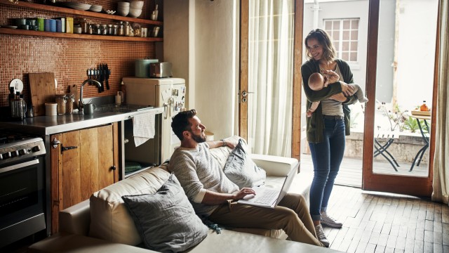 Ein Paar mit Baby freut sich über das Wohnzimmer ihrer neuen Wohnung