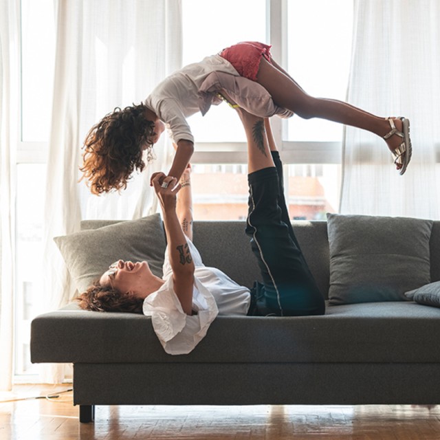 Ein Frau spielt mit ihrer Tochter auf der Couch und freut sich über die große Auswahl an Darlehensarten für die Finanzierung ihres Hauses