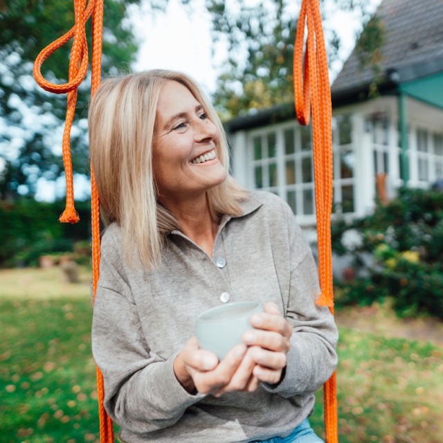Eine Frau sitzt auf einer Schaukel im Garten und freut sich über die Zuschüsse für ihre Sanierung Eine Frau sitzt auf einer Schaukel im Garten und freut sich über die Zuschüsse für ihre Sanierung