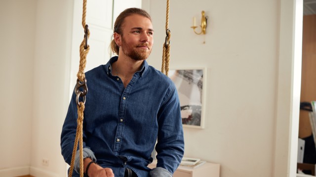 Ein junger Mann sitzt in der Schaukel seines ersten Hauses, welches er mit einem Bausparvetrag finanziert hat