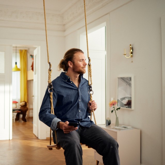 Ein Mann sitzt in einer Schaukel und informiert sich auf seinem Smartphone über das Annuitätendarlehen