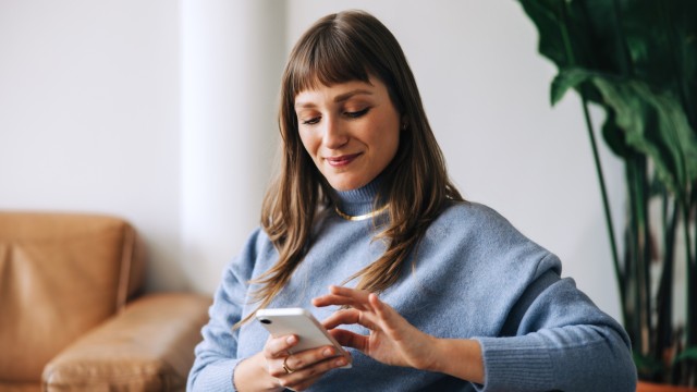 Eine junge Frau informiert sich auf den Smartphone über mögliche Fehler bei einer Baufinanzierung