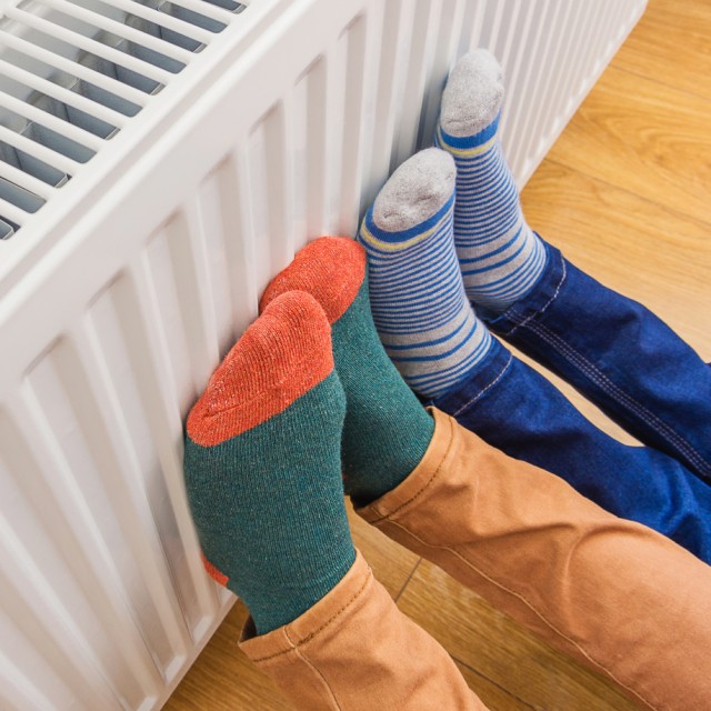 Füße werden an einem Heizkörper gewärt, der mit einer Wärmepumpe betrieben wird