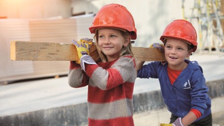 Jetzt Baukindergeld beantragen! Auf einer Baustelle tragen zwei Kinder einen Holzbalken auf der Schulter