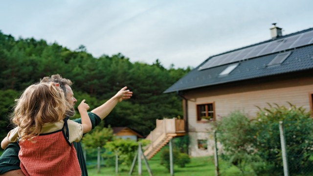 Ein Vater und seine Tochter zeigen auf die neue Solaranlage auf ihrem Dach, die sie bei einer Modernisierung eingebaut haben Ein Vater und seine Tochter zeigen auf die neue Solaranlage auf ihrem Dach, die sie bei einer Modernisierung eingebaut haben