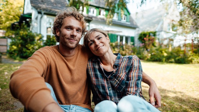 Ein junges Paar im Garten eines Hauses, das es mit Hilfe der Eigenheimrente finanziert hat