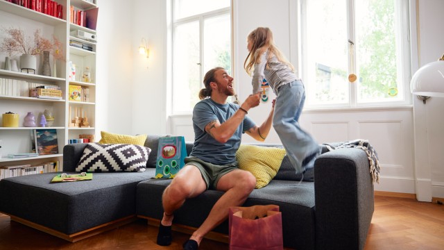 Ein Vater spielt mit seiner Tochter auf der Couch in einer Wohnung, die mit einem Volltilgerdarlehens finanziert wurde Ein Vater spielt mit seiner Tochter auf der Couch in einer Wohnung, die mit einem Volltilgerdarlehens finanziert wurde