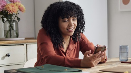 Frau sitzt am Küchentisch und sieht sich auf ihrem Handy die Zinsen für ein Tagesgeldkonto an.
