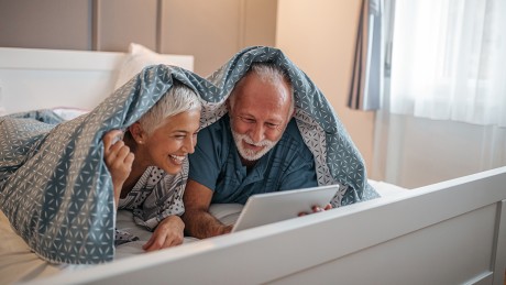 Seniorenpaar liegt auf dem Bett und schauf auf Laptop