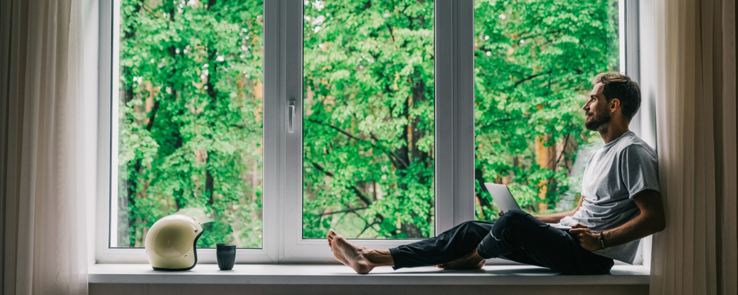 Ein Mann sitzt am Fenster und berechnet seinen Immobilienwert auf dem Laptop Ein Mann sitzt am Fenster und berechnet seinen Immobilienwert auf dem Laptop