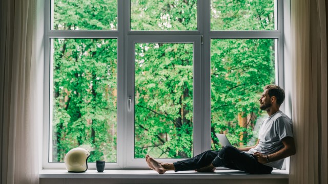 Ein Mann sitzt am Fenster und nutzt den Nebenkostenrechner am Laptop Ein Mann sitzt am Fenster und nutzt den Nebenkostenrechner am Laptop