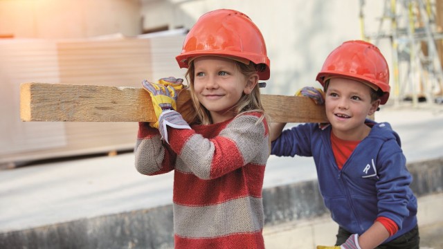 Zwei Kinder tragen lachend einen Holzbalken Auf einer Baustelle tragen zwei Kinder einen Holzbalken auf der Schulter