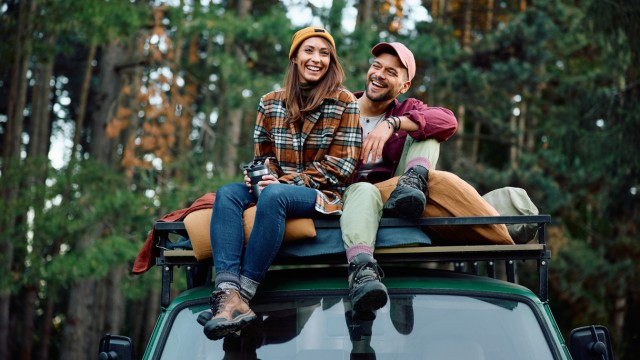 Paar im Campingurlaub sitzt auf dem Dach ihres Offroaders Paar im Campingurlaub sitzt auf dem Dach ihres Offroaders