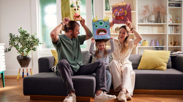 Eine junge Familie spielt auf der Couch in einer Wohnung, die sie mit einem Vorausdalrehen finanziert hat Eine junge Familie spielt auf der Couch in einer Wohnung, die sie mit einem Vorausdalrehen finanziert hat