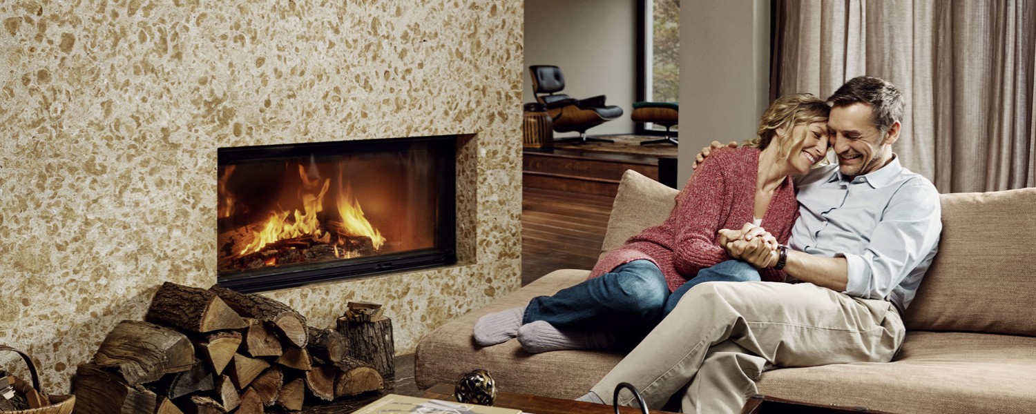 Ein Mann und eine Frau sitzen auf der Couch am Feuer, nachdem Sie Ihre Anschlussfinanzierung abgeschlossen haben Paar vorm Kamin