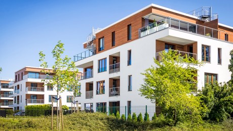 Mit dem Wüstenrot Finanzierungszertifikat höhere Chancen auf die Wunschimmobilie erhalten Moderne Mehrfamilienimmobilien in grüner Anlage vor blauem Himmel