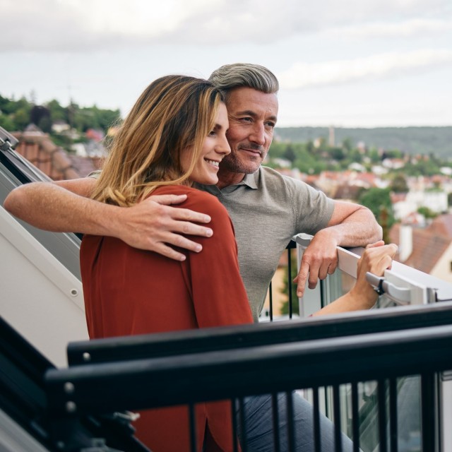 Ein Paar schaut aus Ihrer Dachgeschosswohnung, das es mit einem Annuitätendarlehen finanziert hat Ein Paar schaut aus Ihrer Dachgeschosswohnung, das es mit einem Annuitätendarlehen finanziert hat
