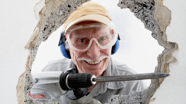 Wartungsarbeiten Mit dem Kopf durch die Wand - Alter Mann bricht mit Bohrmeißel durch Wand